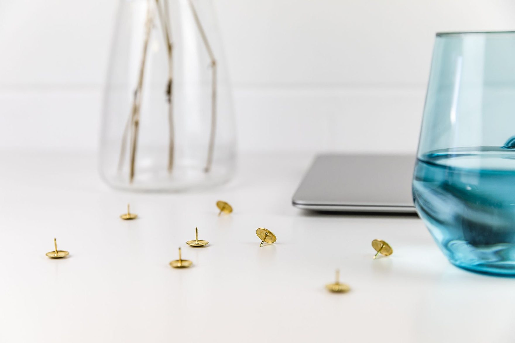 A glass vase, blue glass and gold pins beside a closed laptop
